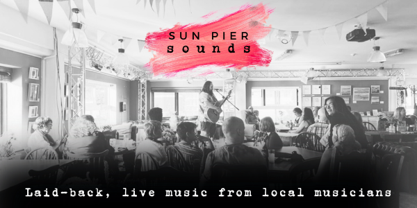 Black and white photo of a man playing a guitar on a stage at Sun Pier Sounds - live music in Medway with the Sun Pier Sounds logo - a pink paint splash on a black background with text overlaid and text reading laid-back, live music from local musicians
