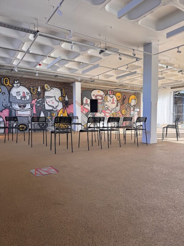 A photo of The Creation Space - a bare wall with colourful graffiti art and chairs set up for a book reading